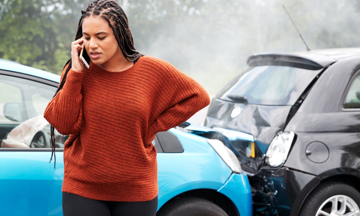 a woman standing next to a car accident on a phone call