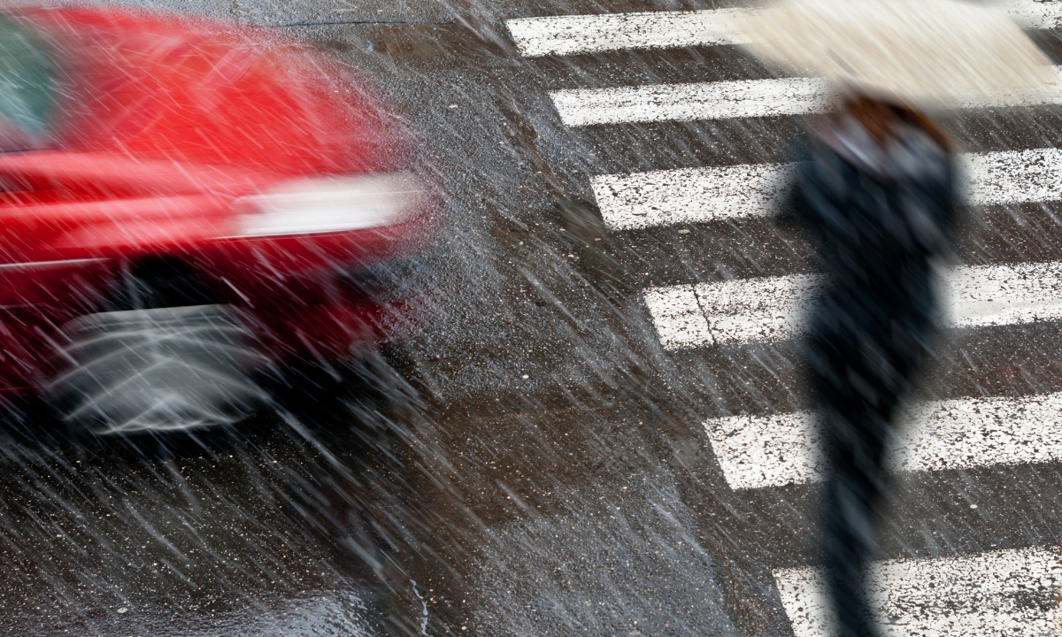 an image blurred by rain with a person under an umbrella on a crosswalk about to be hit by a car